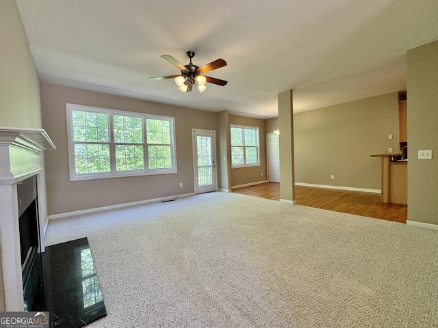 unfurnished living room featuring a fireplace with flush hearth, carpet flooring, baseboards, visible vents, and a ceiling fan
