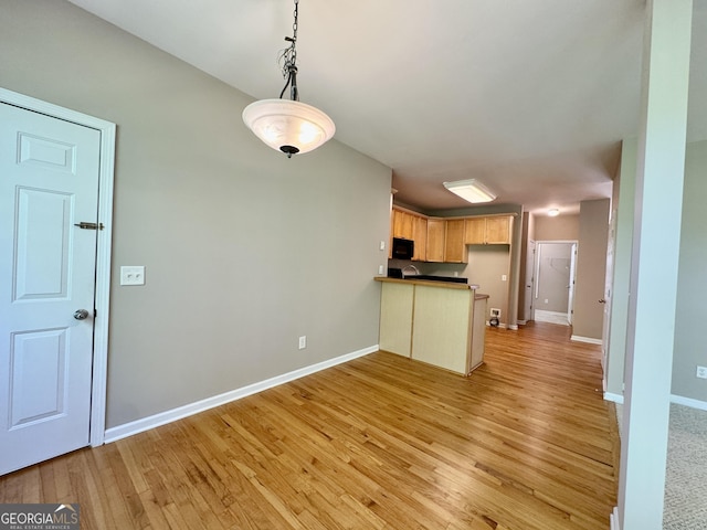 kitchen featuring a peninsula, light wood-style floors, black microwave, and baseboards
