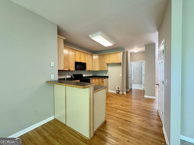 kitchen with a peninsula, light wood finished floors, baseboards, and black appliances
