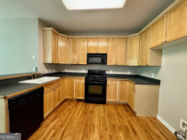 kitchen featuring a peninsula, a sink, dark countertops, light wood-style floors, and black appliances