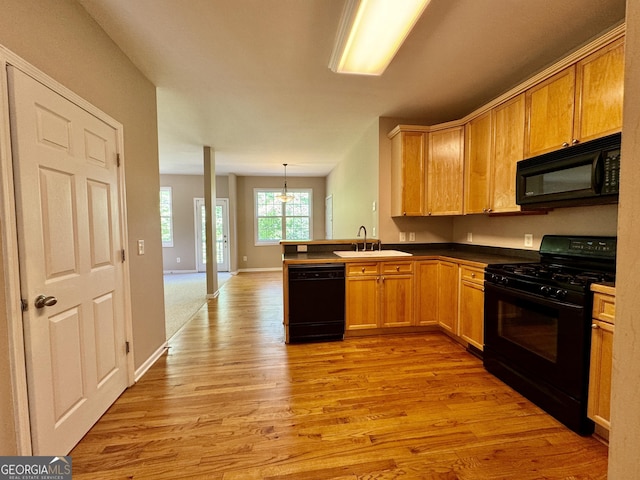 kitchen with dark countertops, a sink, black appliances, light wood-type flooring, and a peninsula