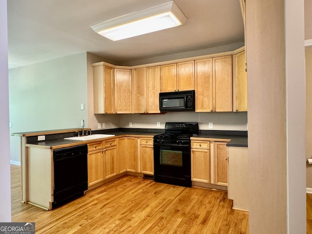 kitchen featuring light wood-type flooring, dark countertops, a sink, and black appliances