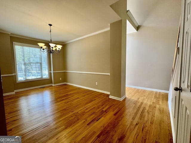 spare room featuring wood finished floors, a notable chandelier, baseboards, and ornamental molding