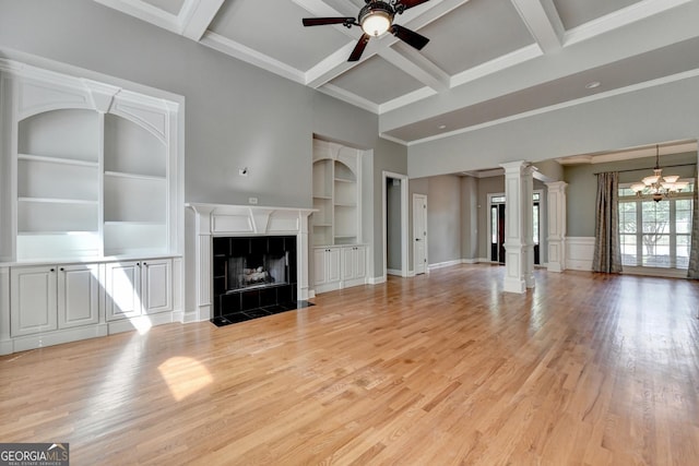 unfurnished living room featuring decorative columns, built in features, a tile fireplace, ceiling fan with notable chandelier, and light wood finished floors