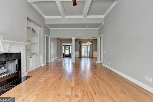 unfurnished living room with beam ceiling, baseboards, ornate columns, a tile fireplace, and light wood finished floors