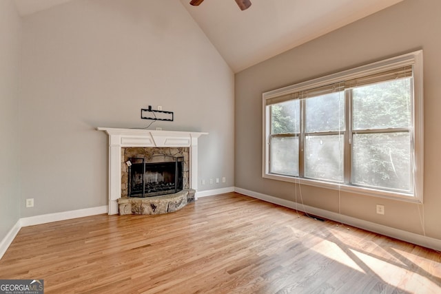 unfurnished living room featuring a ceiling fan, a stone fireplace, wood finished floors, baseboards, and high vaulted ceiling