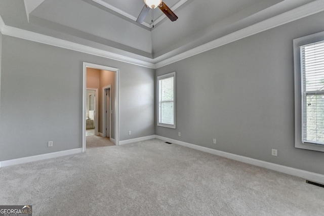 empty room featuring a healthy amount of sunlight, a ceiling fan, light colored carpet, visible vents, and a tray ceiling