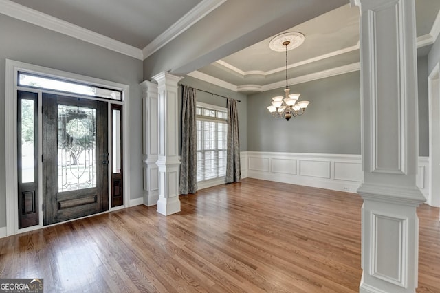 foyer entrance with light wood-style floors, an inviting chandelier, ornamental molding, and ornate columns