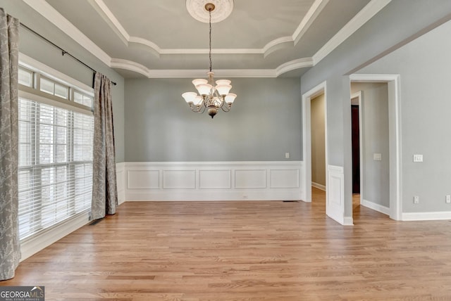 unfurnished dining area with an inviting chandelier, a raised ceiling, crown molding, and light wood-style flooring