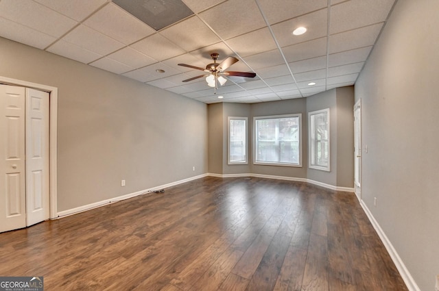 interior space with baseboards, dark wood finished floors, ceiling fan, and a drop ceiling