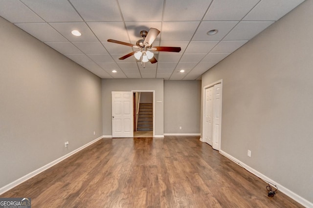 spare room featuring stairs, baseboards, dark wood-type flooring, a paneled ceiling, and a ceiling fan