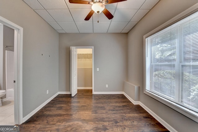 unfurnished bedroom with a drop ceiling, multiple windows, wood finished floors, and a spacious closet