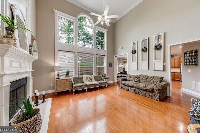 1738 Honey Tree Pl, Hoschton, GA 30548 - living area with a ceiling fan, a towering ceiling, wood finished floors, crown molding, and a fireplace with raised hearth