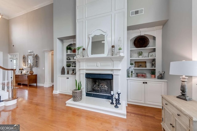 1738 Honey Tree Pl, Hoschton, GA 30548 - living area featuring a towering ceiling, light wood-type flooring, built in features, a fireplace with raised hearth, and crown molding