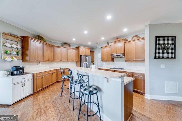1738 Honey Tree Pl, Hoschton, GA 30548 - kitchen with under cabinet range hood, gas cooktop, stainless steel fridge with ice dispenser, ornamental molding, and light wood-type flooring