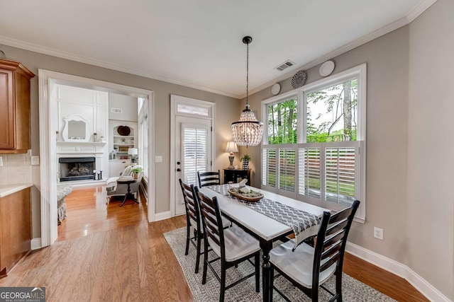 1738 Honey Tree Pl, Hoschton, GA 30548 - dining space with light wood-type flooring, ornamental molding, a fireplace with raised hearth, and a chandelier