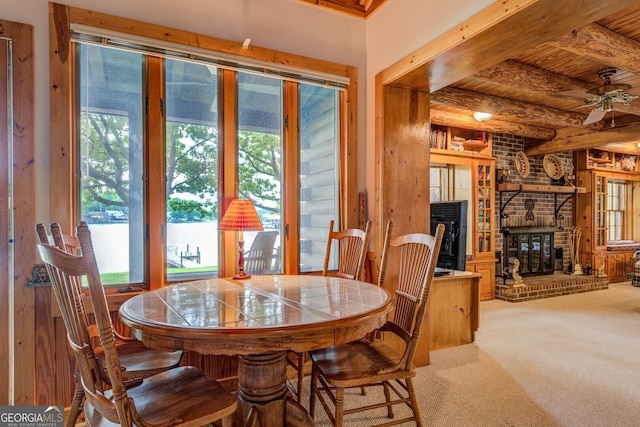 carpeted dining space featuring wood ceiling, ceiling fan, a brick fireplace, and beam ceiling