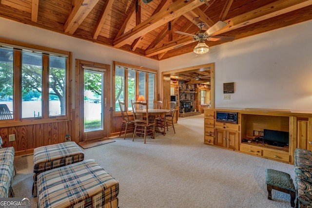 living room with lofted ceiling with beams, wooden ceiling, light carpet, and a stone fireplace