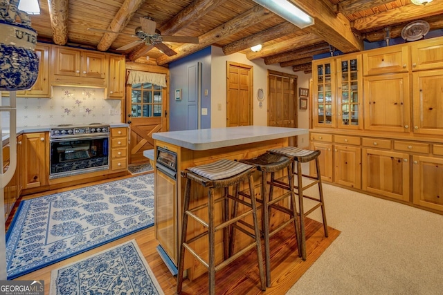 kitchen featuring ceiling fan, light countertops, wooden ceiling, a kitchen island, and beamed ceiling