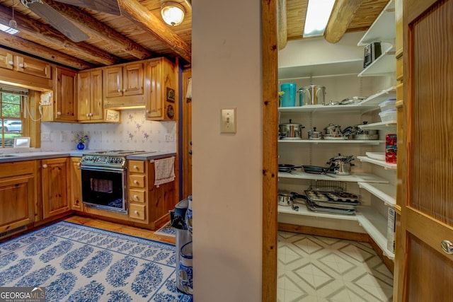 kitchen featuring light countertops, brown cabinetry, beam ceiling, and stainless steel range with electric stovetop