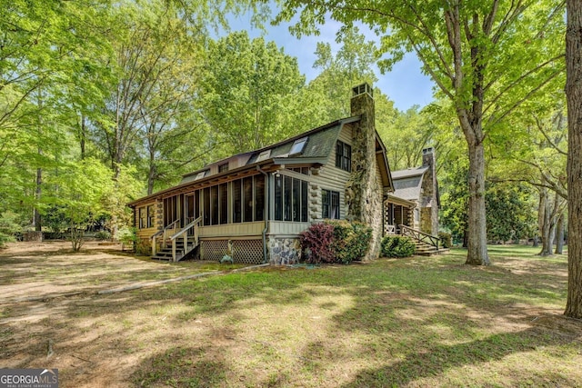 view of home's exterior with a yard, a chimney, and a sunroom