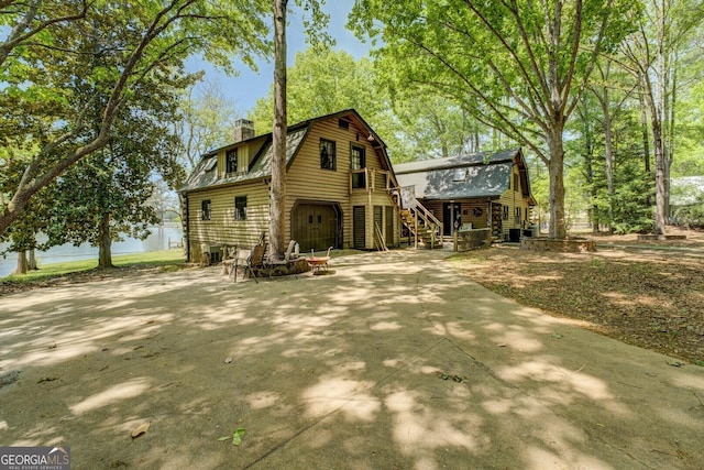 view of front facade with a garage, a gambrel roof, a chimney, stairs, and log siding