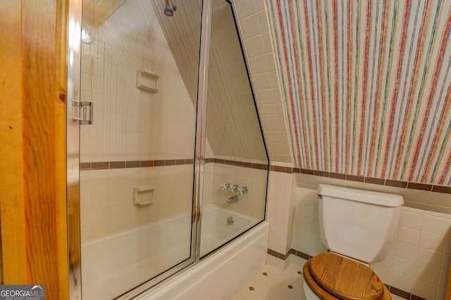 bathroom with enclosed tub / shower combo, wainscoting, toilet, and tile walls