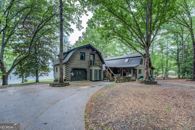 view of front of house with covered porch, driveway, stairway, log exterior, and a gambrel roof