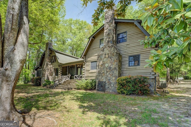 exterior space with central AC unit, a gambrel roof, a chimney, and log siding