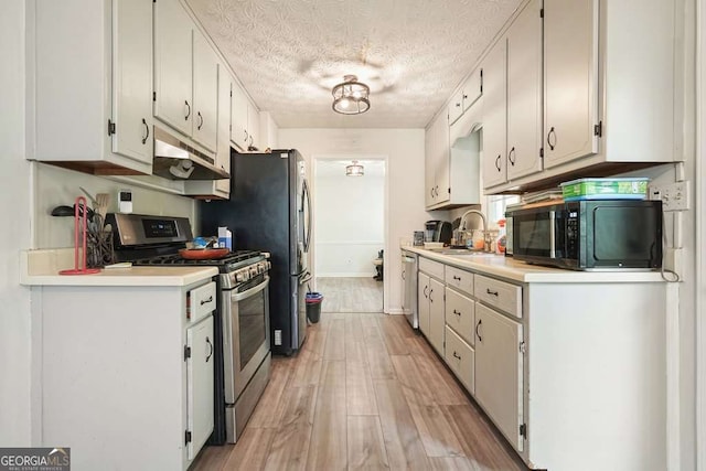 408 Walnut Dr, Woodstock, GA 30189 - kitchen with appliances with stainless steel finishes, a sink, under cabinet range hood, light wood-style flooring, and light countertops