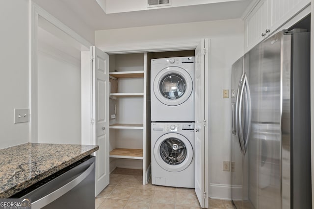 laundry area with stacked washing machine and dryer and light tile patterned floors