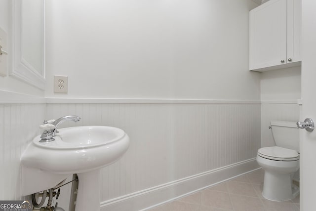 bathroom with tile patterned flooring, a wainscoted wall, toilet, and a sink