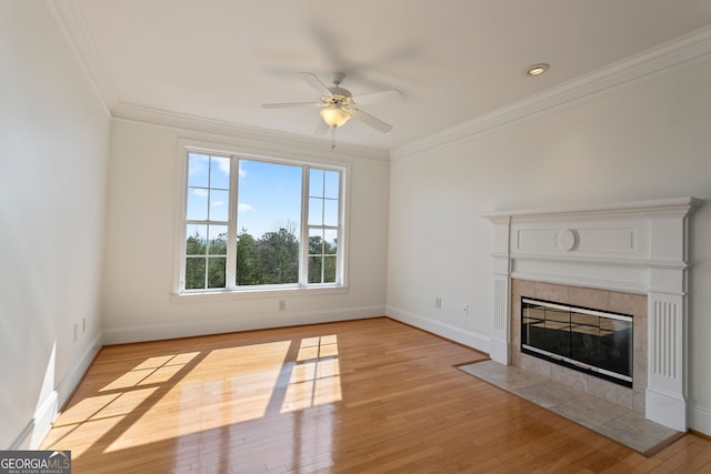 unfurnished living room with a ceiling fan, ornamental molding, a tiled fireplace, light wood finished floors, and baseboards