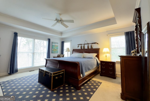 bedroom with ornamental molding, a ceiling fan, light colored carpet, and a tray ceiling