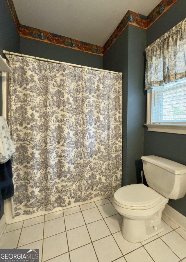 bathroom with toilet, a shower with shower curtain, tile patterned flooring, and baseboards