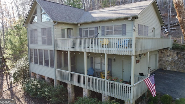 rear view of property featuring a garage, aphalt driveway, a shingled roof, and a sunroom