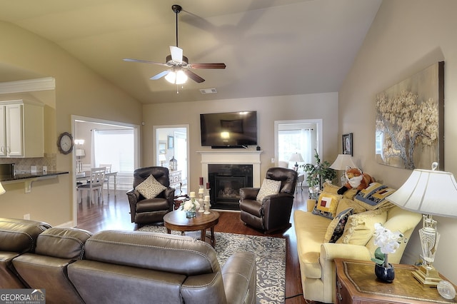living room featuring a glass covered fireplace, a ceiling fan, visible vents, vaulted ceiling, and wood finished floors