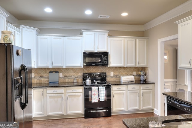 kitchen with dark stone counters, white cabinetry, visible vents, light wood-style floors, and black appliances