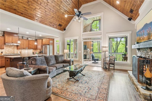 living room featuring a stone fireplace, wood ceiling, high vaulted ceiling, light wood finished floors, and a ceiling fan
