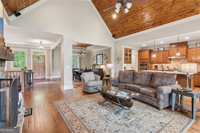 living area with high vaulted ceiling, a ceiling fan, plenty of natural light, wooden ceiling, and wood finished floors