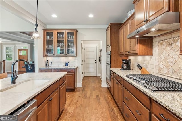 kitchen with under cabinet range hood, a sink, brown cabinets, hanging light fixtures, and glass insert cabinets
