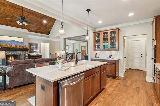 kitchen featuring appliances with stainless steel finishes, a sink, lofted ceiling, a fireplace, and brown cabinetry