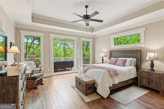 bedroom featuring a raised ceiling, access to exterior, wood-type flooring, ornamental molding, and ceiling fan