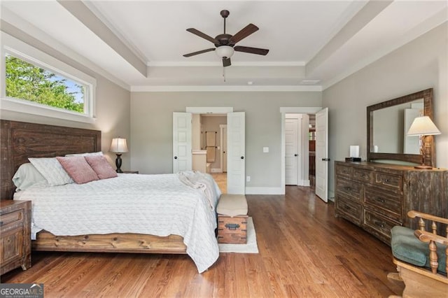 bedroom featuring a tray ceiling, wood finished floors, ornamental molding, baseboards, and a ceiling fan