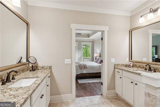 ensuite bathroom featuring baseboards, two vanities, and ornamental molding