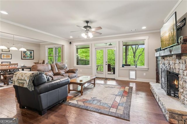 living room featuring healthy amount of natural light, a stone fireplace, a ceiling fan, crown molding, and hardwood / wood-style floors