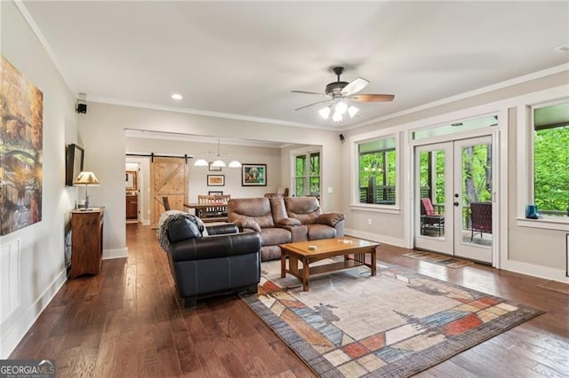 living area featuring a barn door, wood-type flooring, crown molding, a ceiling fan, and baseboards