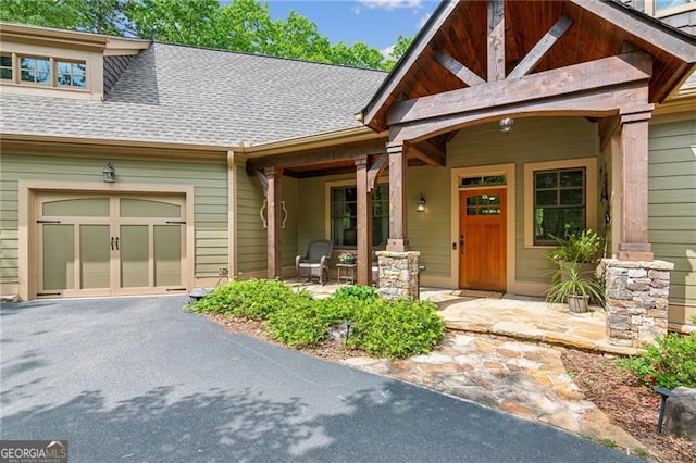view of exterior entry featuring a porch, roof with shingles, driveway, and a garage