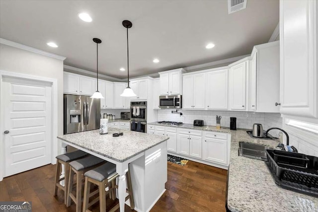 kitchen with a center island, visible vents, white cabinetry, ornamental molding, and appliances with stainless steel finishes