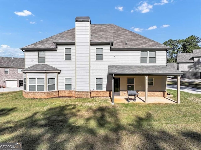 rear view of house featuring a lawn, a chimney, a shingled roof, and a patio